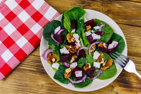 Tasty spinach salad with boiled beetroot, feta cheese, walnut and red onion on wooden table. Top view. Healthy vegetarian foodの写真素材