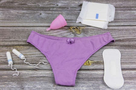 Women's panties with menstrual cups, sanitary pads and tampons on wooden background. Concept of critical days, menstruation, feminine hygieneの写真素材