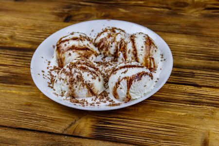 Vanilla ice cream with chocolate topping in white plate on a wooden table