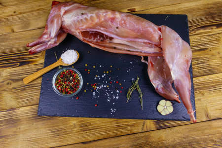 Whole raw rabbit meat with spices on a black slate cutting board on wooden table. Top viewの写真素材