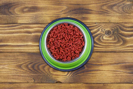 Dry food for cat or dog in bowl on wooden background. Pet food on wood surface. Top viewの写真素材