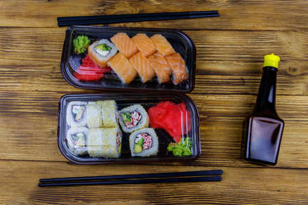 Set of sushi rolls in plastic boxes, soy sauce and chopsticks on wooden table. Top view. Sushi for take away or delivery of sushi in plastic containersの写真素材