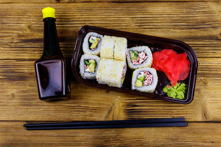 Uramaki sushi rolls with surimi in plastic box on wooden table. Top view. Sushi for take away or delivery of sushi in plastic containerの写真素材
