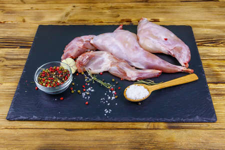 Raw rabbit legs with spices on a black slate cutting board on wooden tableの写真素材