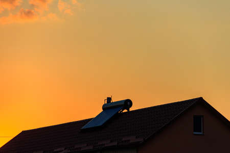 Solar water heater on a residential house rooftop at sunset. Renewable energy for house