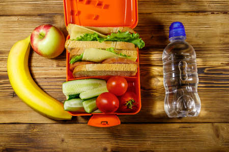 Bottle of water, apple, banana and lunch box with sandwiches and fresh vegetables on a wooden table. Top viewの写真素材