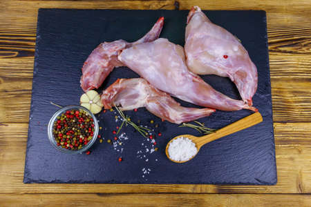 Raw rabbit legs with spices on a black slate cutting board on wooden table. Top viewの写真素材