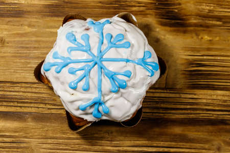 Christmas cake decorated with white glaze and snowflake on wooden table. Top view