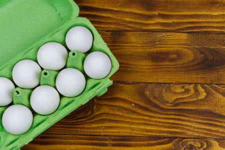 Raw chicken eggs in cardboard egg box on wooden table. Top view