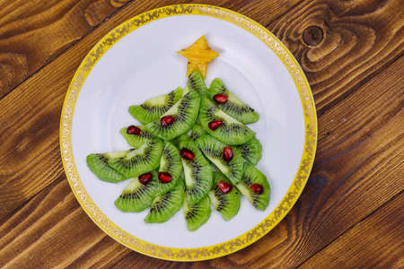 Christmas tree made of kiwi slices and pomegranate on wooden table. Top view. Creative idea for Christmas and New Year festive desserts. Funny food idea for kidsの写真素材