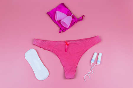 Women's panties with menstrual cups, sanitary pads and tampons on pastel pink background. Top view. Concept of critical days, menstruation, feminine hygieneの写真素材