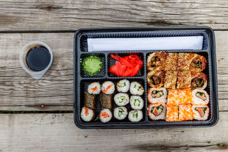 Set of sushi rolls in plastic box on wooden table. Sushi for take away or delivery of sushi in plastic container. Top viewの写真素材