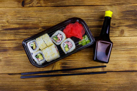 Uramaki sushi rolls with surimi in plastic box on wooden table. Top view. Sushi for take away or delivery of sushi in plastic containerの写真素材