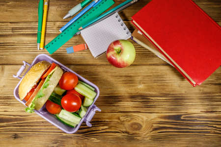 Back to school concept. School supplies, books, apple and lunch box with burgers and fresh vegetables on a wooden table. Top viewの写真素材