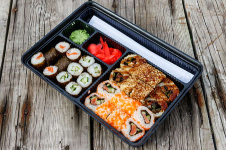 Set of sushi rolls in plastic box on wooden table. Sushi for take away or delivery of sushi in...