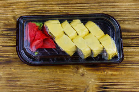 Sushi cheese rolls in plastic box on wooden table. Top view. Sushi for take away or delivery of sushi in plastic containerの写真素材