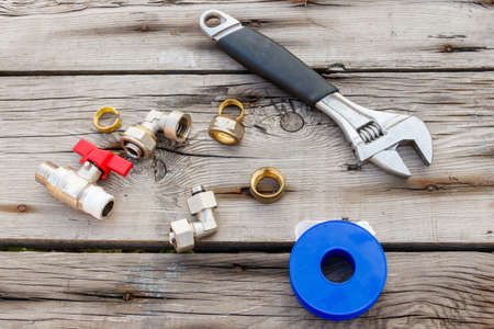 Various plumbing spare parts, sealing tape and adjustable wrench on rustic wooden background. Top viewの写真素材