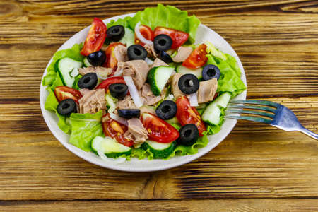 Tasty tuna salad with lettuce, black olives and fresh vegetables on wooden tableの写真素材