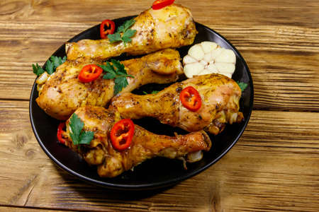 Roasted chicken drumsticks with spices in a black plate on a wooden tableの写真素材