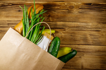 Paper bag with different food on wooden table. Top view. Grocery shopping conceptの写真素材