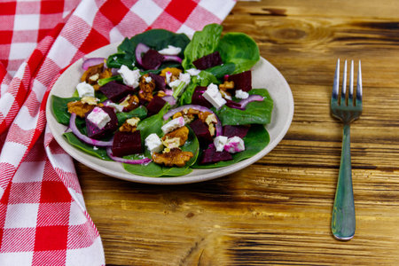 Tasty spinach salad with boiled beetroot, feta cheese, walnut and red onion on wooden table. Healthy vegetarian foodの写真素材