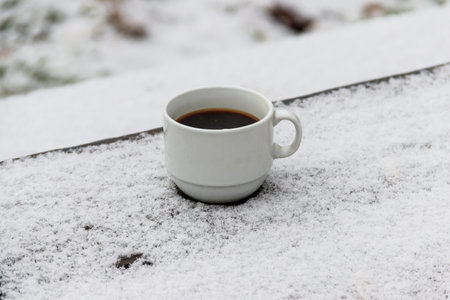 Cup of coffee on a snow covered table at winterの写真素材