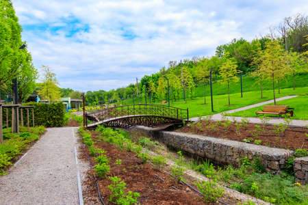 Beautiful view of the city park with arched footbridge across small river and young treesの写真素材