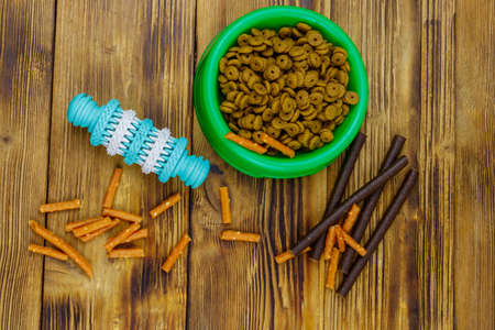 Dog toy, delicacy food and feed for dogs in green plastic bowl on wooden background. Top view. Dog care conceptの写真素材