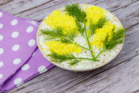 Traditional russian layered salad Mimosa decorated with sprigs of mimosa (made of eggs yolk and dill) on wooden tableの写真素材