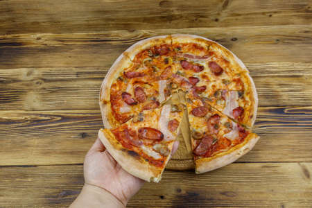Hand taking a slice of tasty pizza. Hot italian pizza on wooden table. Top viewの写真素材