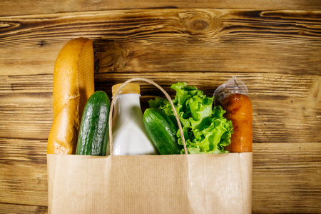 Paper bag with different food on wooden table. Top view. Grocery shopping conceptの写真素材