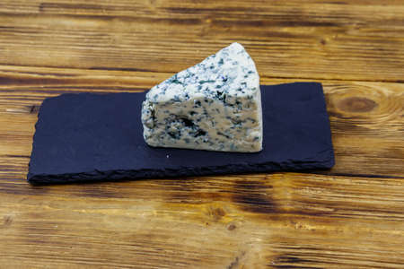 Blue cheese with mold on serving black slate board on wooden tableの写真素材