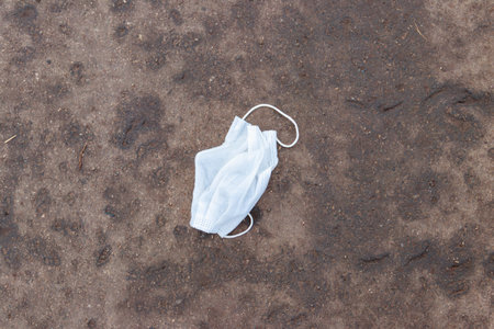 Dirty used disposable medical face mask dumped as garbage on asphalt street. Waste during  pandemicの写真素材