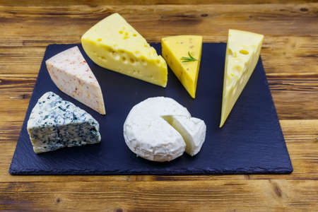Set of various types of cheese on black slate board on a wooden tableの写真素材