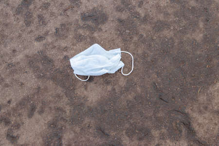 Dirty used disposable medical face mask dumped as garbage on asphalt street. Waste during COVID-19. Pollution due coronavirus pandemicの写真素材