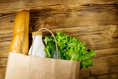 Paper bag with different food on wooden table. Top view. Grocery shopping concept