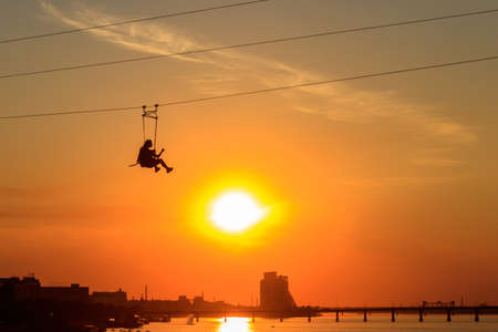 Silhouette of young woman on a zipline at sunsetの写真素材