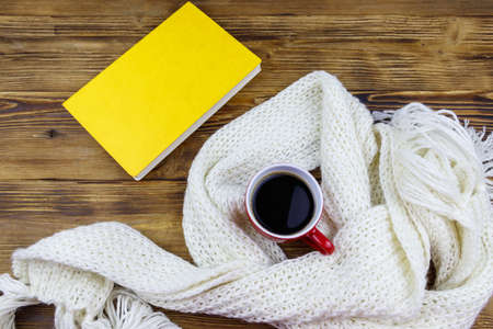 Knitted white scarf, book and cup of coffee on wooden table. Top view. Winter cozy conceptの写真素材