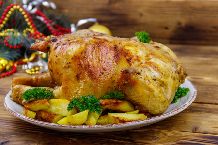 Baked whole chicken with potato and Christmas decorations on a wooden tableの写真素材