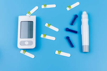 Digital glucometer, lancet pen, disposable needles and test strips on pastel blue background. Top view. Diabetes conceptの写真素材