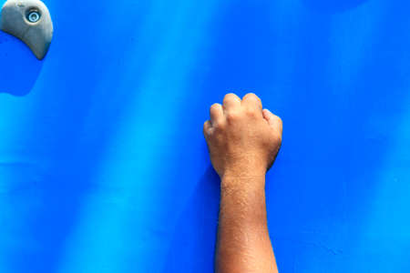 Male climber hand gripping hold on the blue climbing wall