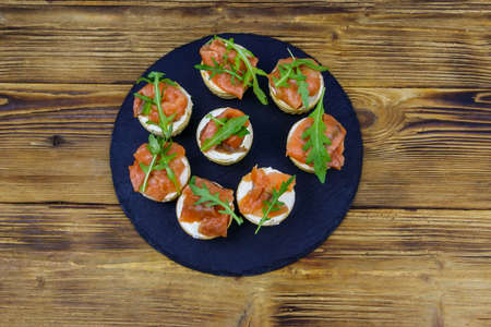 Tartlets with salmon, cream cheese and arugula on wooden table. Top view