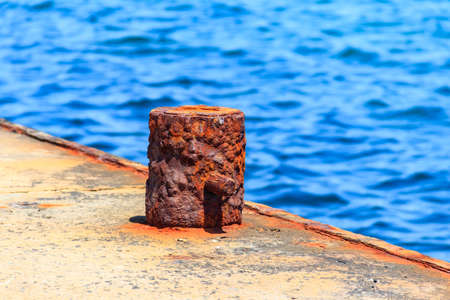 Old rusty mooring bollard by the pier at seaside