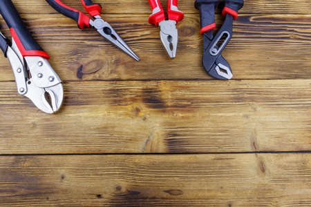 Set of different pliers on wooden background. top view, copy space