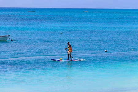 Nungwi, Zanzibar, Tanzania - September 16, 2021: Young black man on stand up paddle board (paddleboard, SUP) paddleboarding in the Indian ocean in Nungwi, Zanzibar, Tanzaniaのeditorial素材
