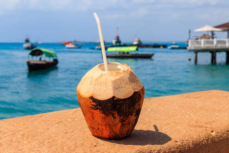 Fresh tropical coconut cocktail with drinking straw by ocean in Stone Town, Zanzibar, Tanzaniaの写真素材