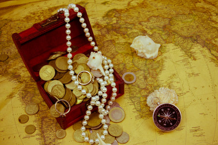 Treasure chest with jewelry and coins, compass and shells on a vintage mapの写真素材