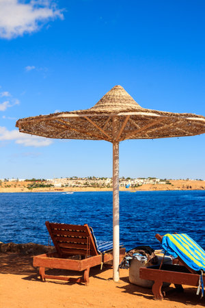 Sun umbrellas and chaise lounges on tropical beach. Concept of rest, relaxation, holidays, resortの写真素材