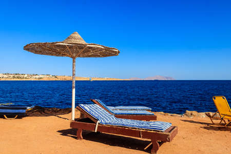 Sun umbrellas and chaise lounges on tropical beach. Concept of rest, relaxation, holidays, resortの写真素材