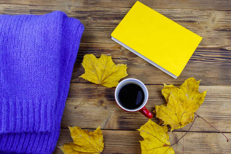 Cozy knitted blue sweater, book, cup of coffee and autumn maple leaves on wooden table. top view. autumn cozy conceptの写真素材